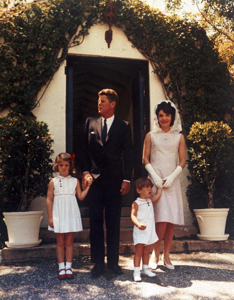A full length portrait of U.S. president John F Kennedy with first lady Jacqueline Kennedy and their children, Caroline and John Jr, standing outside in front of a door at his father Jospeh P Kennedy's estate, Palm Beach, Florida, Easter Sunday, April 14,