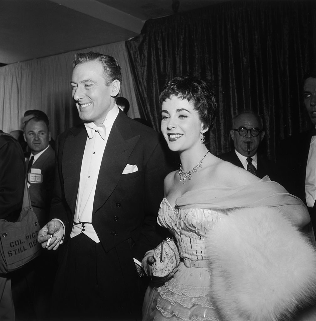 25th March 1954: British-born actor Elizabeth Taylor smiles while walking with her second husband, British actor Michael Wilding (1912-1979), at the Academy Awards, Los Angeles, California. Taylor holds a white fur stole under her arm. Wilding smokes a cigarette. (Photo by Hulton Archive/Getty Images)