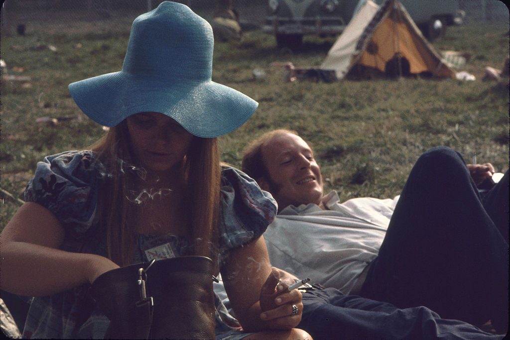 View of an unidentified pair of festival goers on the grass on the grounds of the Woodstock Music and Arts Fair, Bethel, New York, August 1969. The man lies on his back, while the woman, a wide-brimmed floppy hat oh her head and her festival ticket around her neck, smokes and looks through her purse. The festival ran from August 15 to 18. (Photo by Ralph Ackerman/Getty Images)