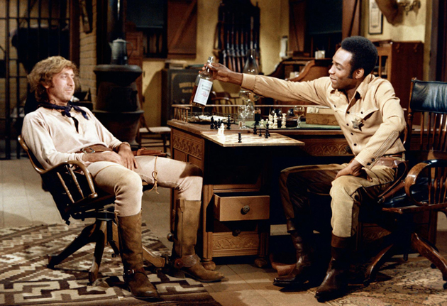Full shot of Cleavon Little as Bart offering whiskey bottle for Gene Wilder as Jim, both seated in sheriff's office. PHOTOGRAPHS TO BE USED SOLELY FOR ADVERTISING, PROMOTION, PUBLICITY OR REVIEWS OF THIS SPECIFIC MOTION PICTURE AND TO REMAIN THE PROPERTY OF THE STUDIO. NOT FOR SALE OR REDISTRIBUTION. ALL RIGHTS RESERVED.