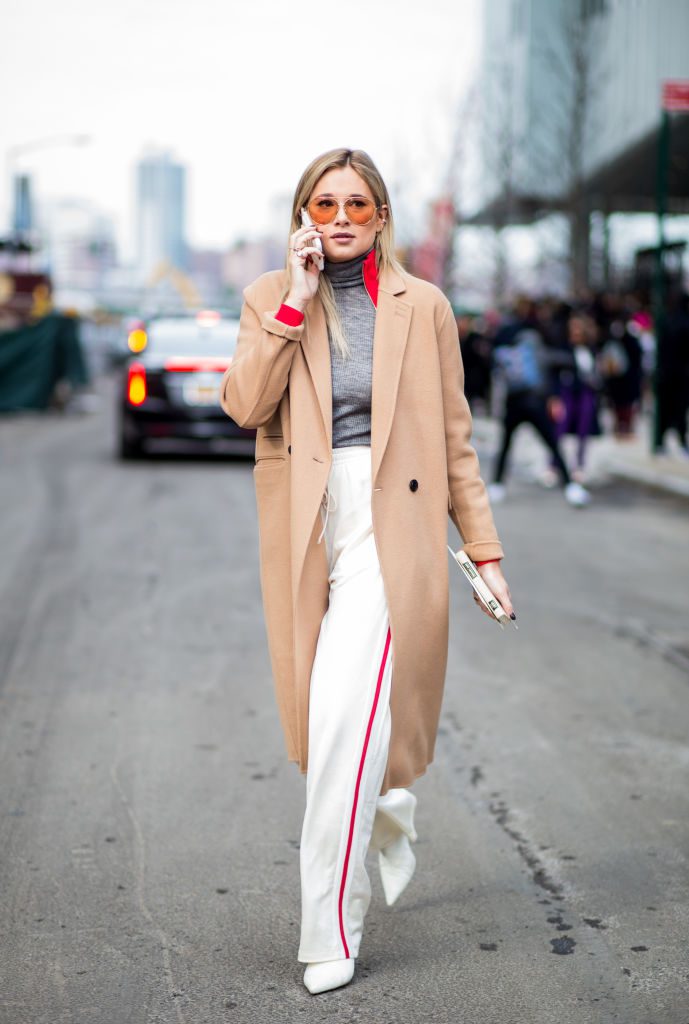 Woman wearing white pants and long camel coat.