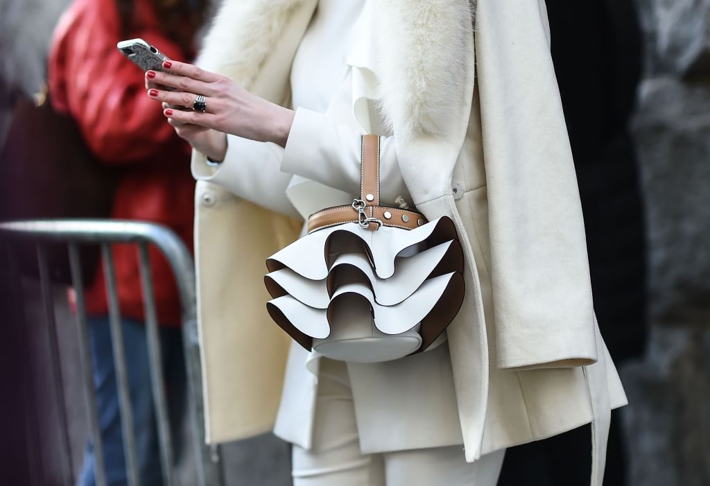 Woman wearing a white coat and white suit, carrying a white handbag.