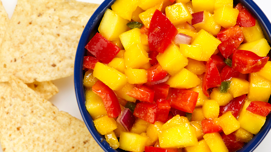 A mango salsa dip with onions and peppers served in a dark blue bowl. 