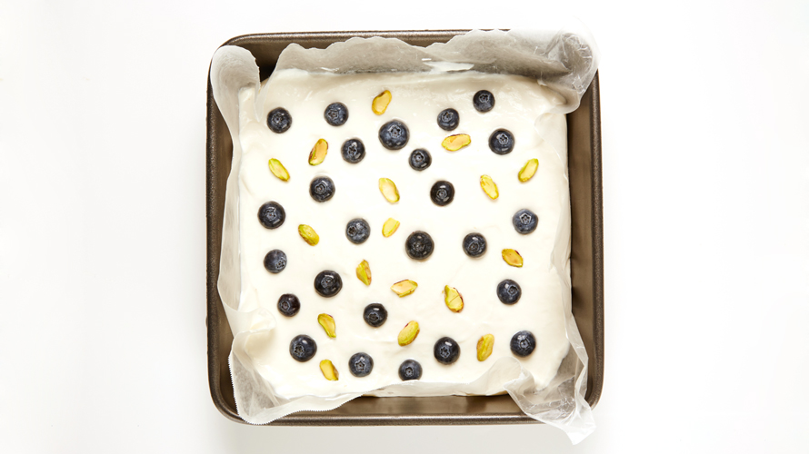 Frozen greek yogurt with blueberries and pistachios on a baking tray.
