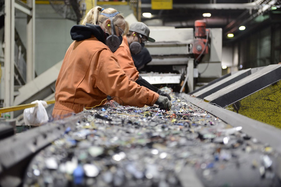 I worker wearing protective eyewear and a breathing apparatus sort through a pile of electronic parts at a recycling plant. 