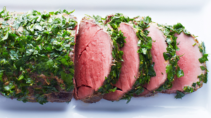 Medium rare horseradish-crusted beef tenderloin with four slices cut and displayed on a white plate. 
