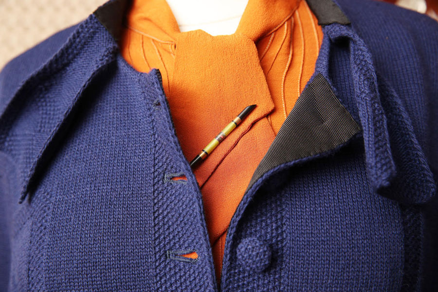 A violet wool jacket with the first two buttons undone displaying a subdued orange scarf. 