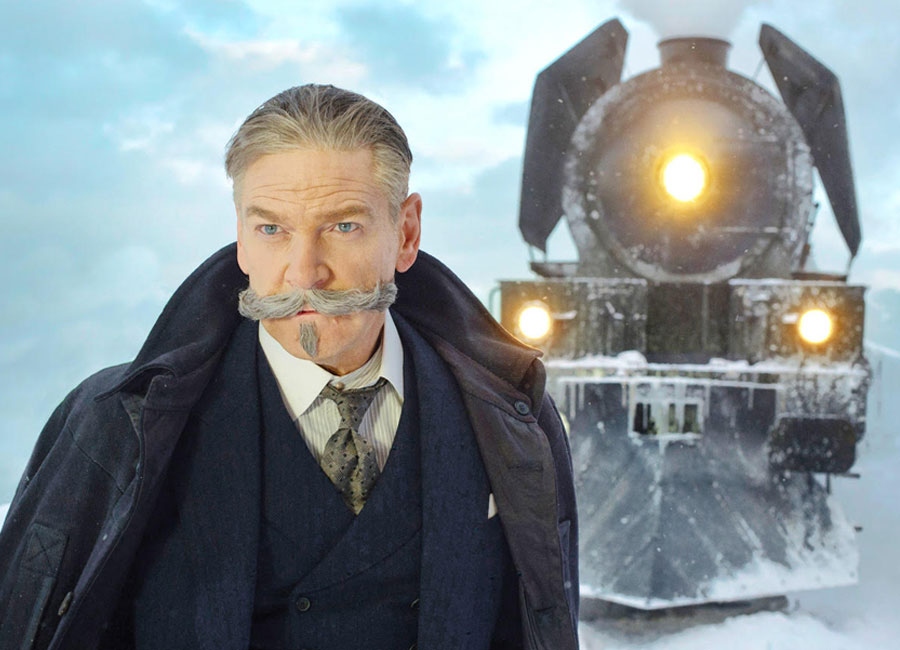 enneth Branagh as Hercule Poirot in Murder On The Orient Express posing in front of the train.