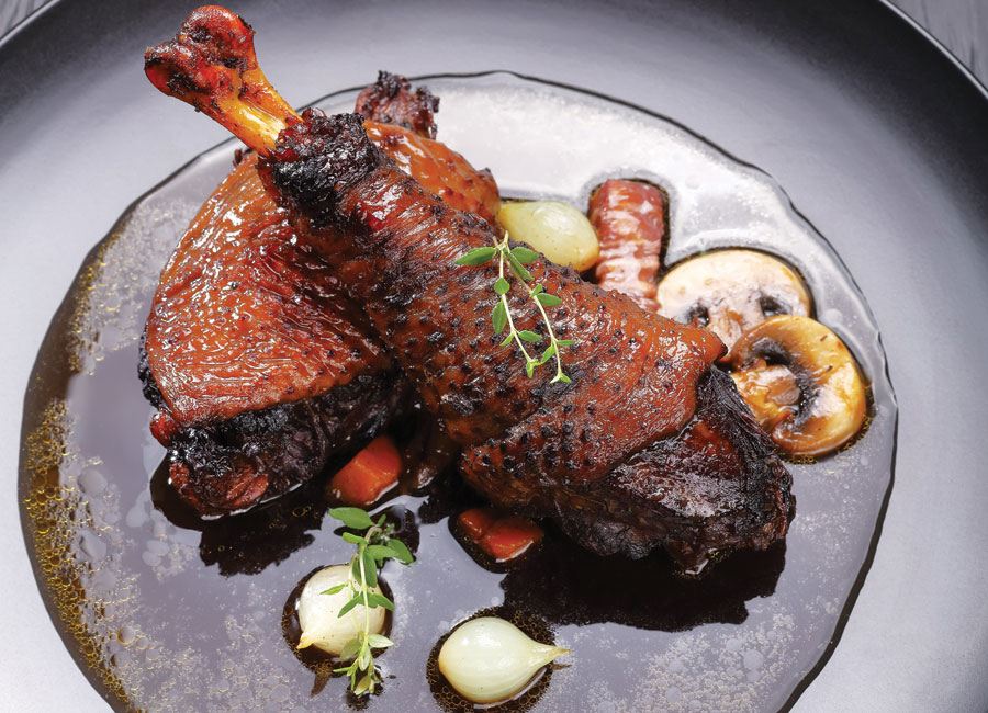 A photo of a chicken leg resting on a bed of vegetables. The dish is called Coq au Vin.