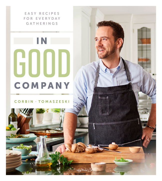 Book cover for In Good Company. Corbin Tomaszeski standing at a kitchen counter and cutting board with freshly chopped mushrooms laying on it. 
