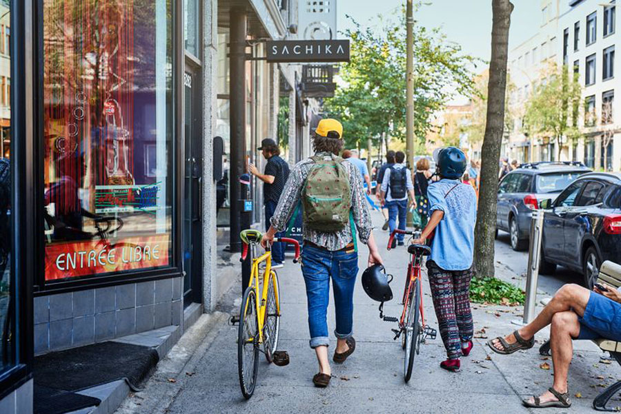 Two locals walk their bike along the sidewalk passing coffee shops in the Mile End neighbourhood in Montreal. 