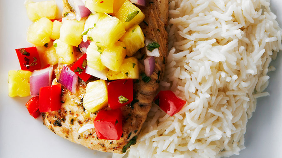 Jerk Fish with pineapple salsa piled on top of it beside a pile of coconut rice. 