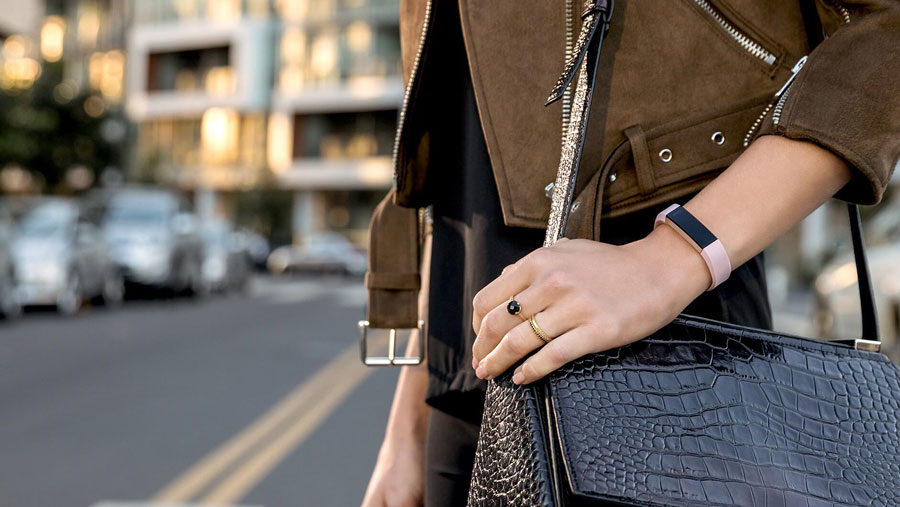 A woman crossing the street wearing a leather purse and a fitness band on her wrist. 