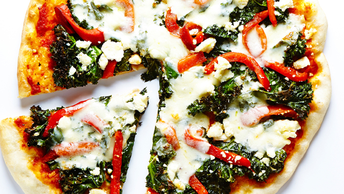  A thin crust pizza with roasted peppers and kale toppings.