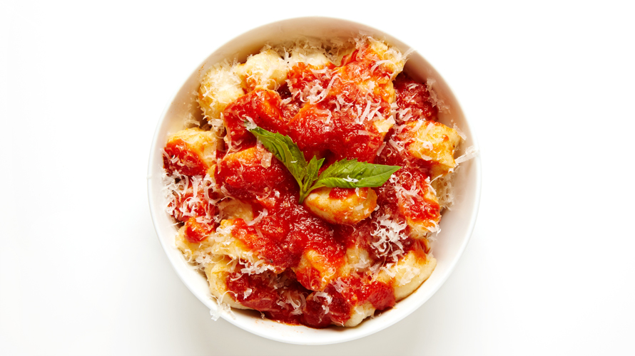 A bowl of pasta with tomato sauce and parmesan on it. 