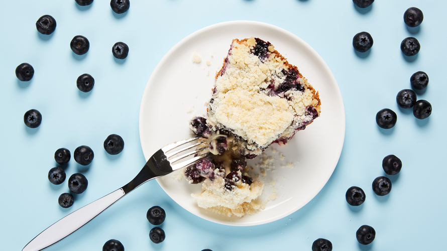 Blue berry cheesecake on a white plate surrounded by blueberries. 