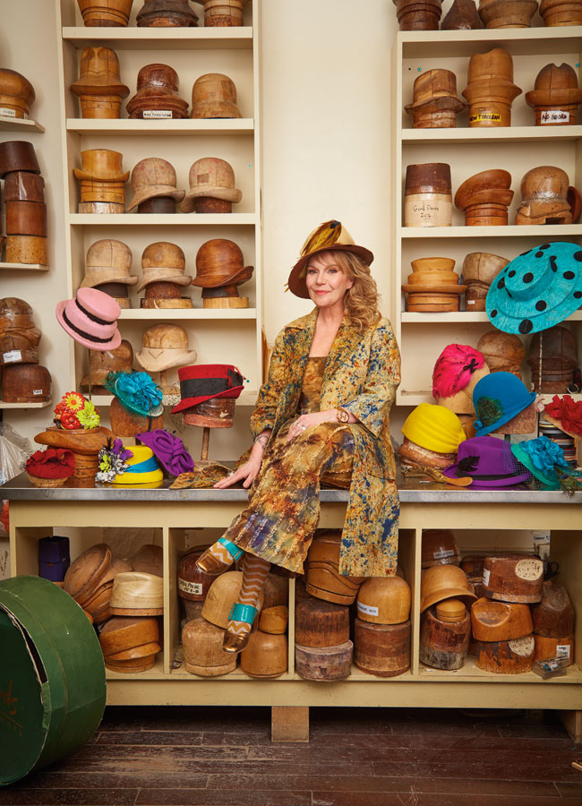 Karyn Ruiz in her shop surrounded by wooden moulds of hats and colourful hats. 