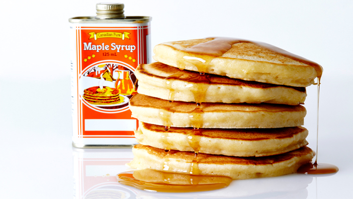 A stack of pancakes with syrup spilling over the sides. 