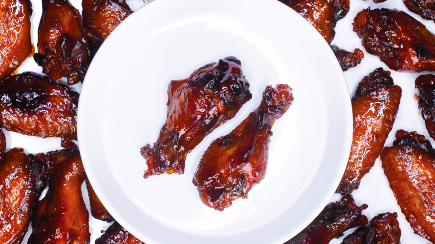 A plate with two sticky honey baked chicken wings surrounded by more chicken wings in the background. 