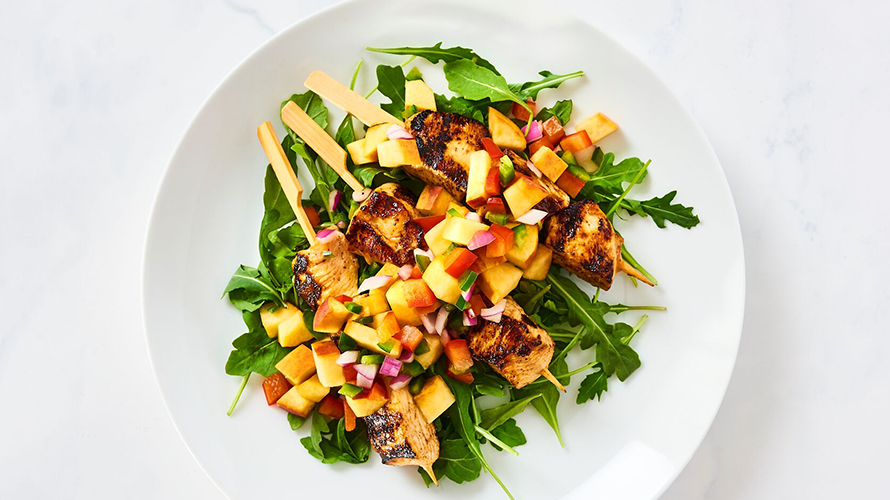 Chicken skewers on a bed of greens with peach salsa on top. 