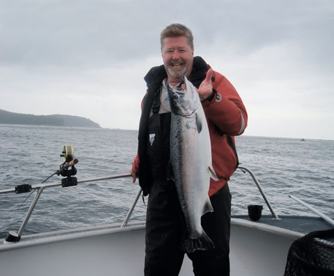 A man smiling as he holds a fish that he caught by the hook. 