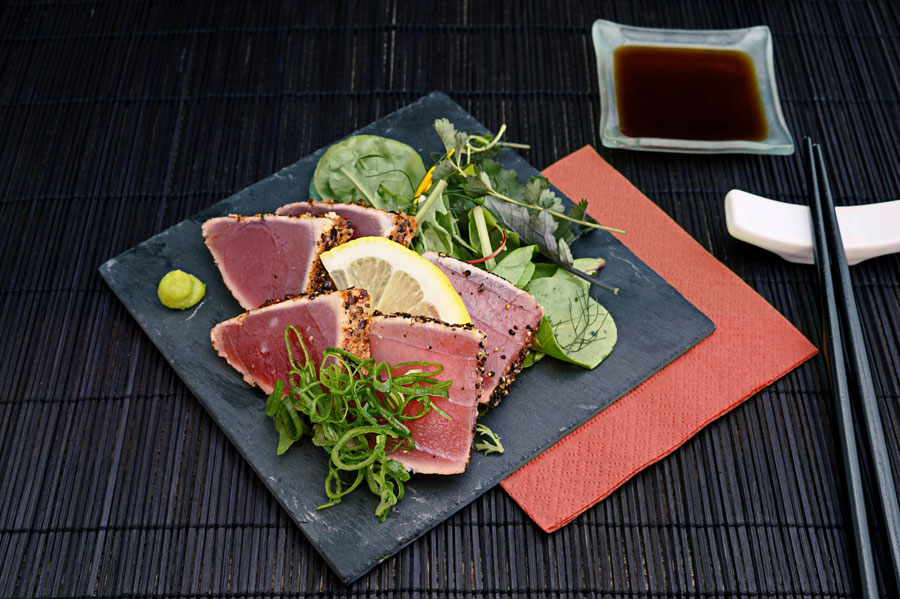 Seared tuna with greens a lemon and a dot of wasabi sauce beside it. 