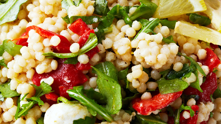 A close up of Couscous salad with tomato and greens. 