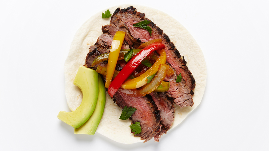 Grilled flank steak on a fajita with red and yellow peppers and avocado. 