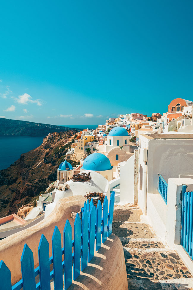 A view of a cliffside town in Santorini featuring multiple spherical roofs and multicoloured structures.