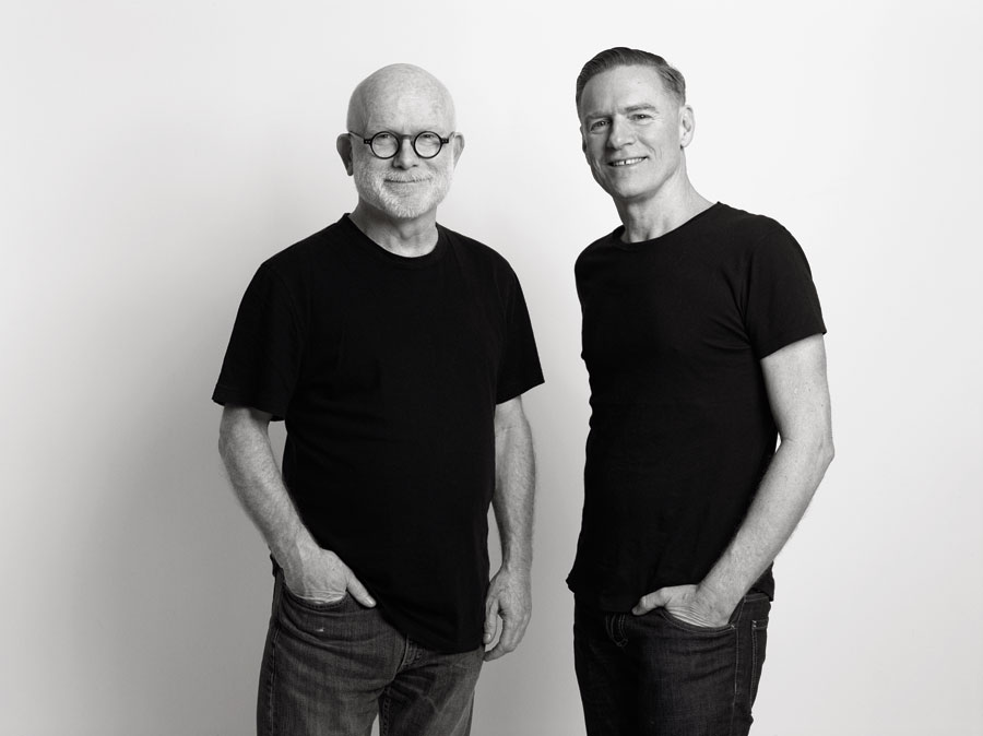 Bryan Adams and Jim Vallance in a black and white photo wearing black t-shirts each with one hand in their pocket.
