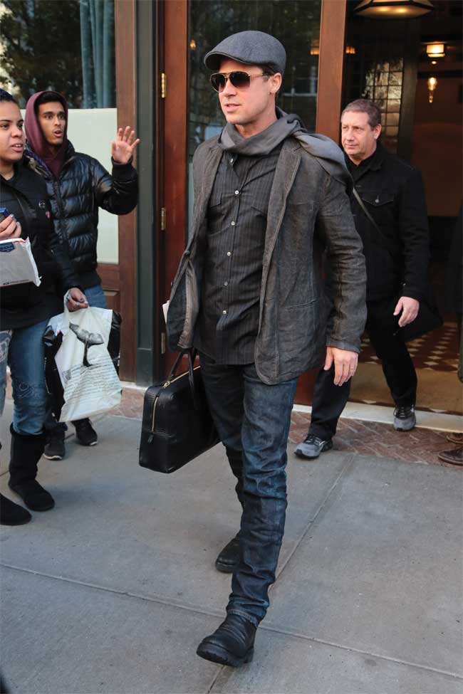 Brad Pitt in a newspaper boys hat wearing dark clothing. 