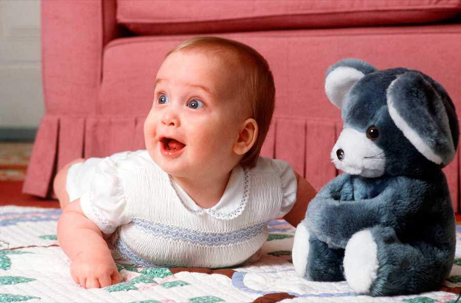 Prince William as an infant posing beside a stuffed bear.