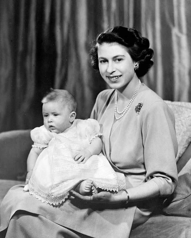 Prince Charles as an infant in a white nightgown sitting on his mother's lap.