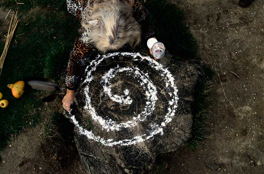 A grey-haired woman pouring salt in a spiral pattern on a dark wooded floor. 