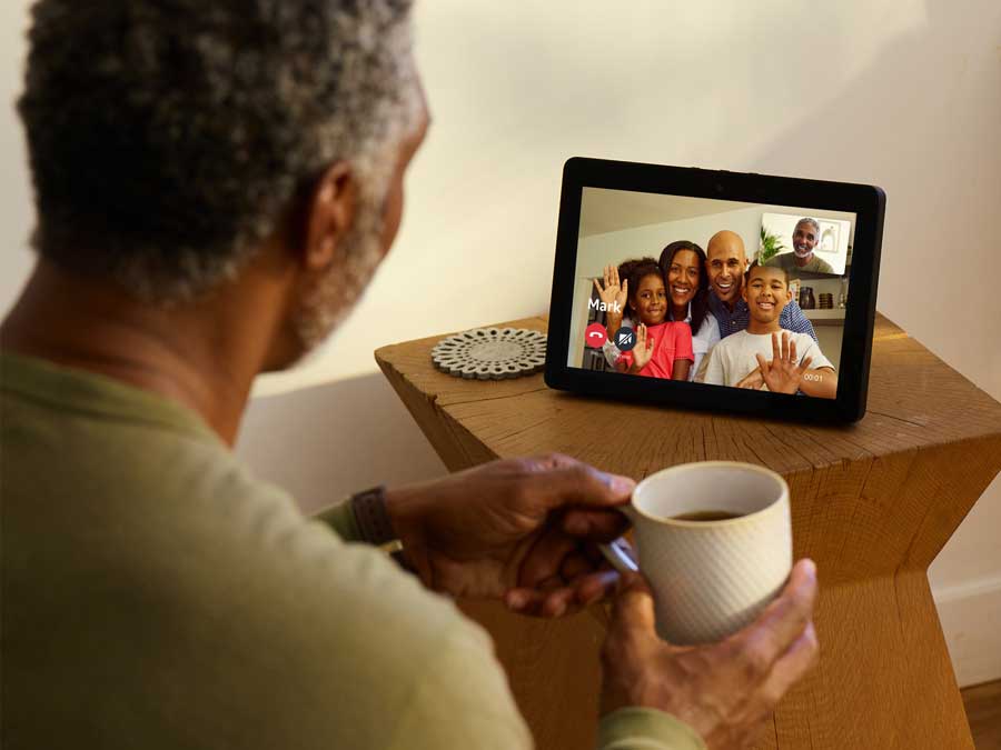 A man looking at a tablet-like screen with several of his family members on it.