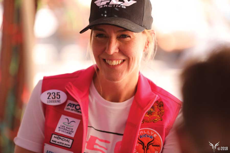 A woman smiling wearing a black hat and red racing vest.