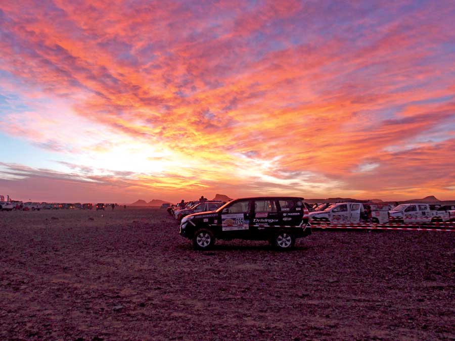A truck sitting at the starting line with the a glowing sunset of pink, purple and orange in the background. 