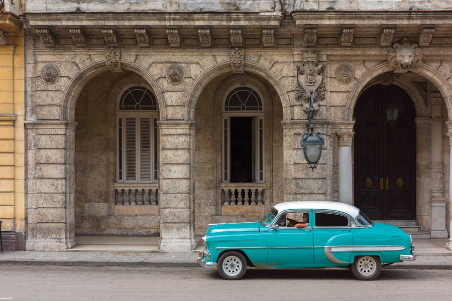 A turquoise 1960s style car sitting in front of an old building in Old Havana. 