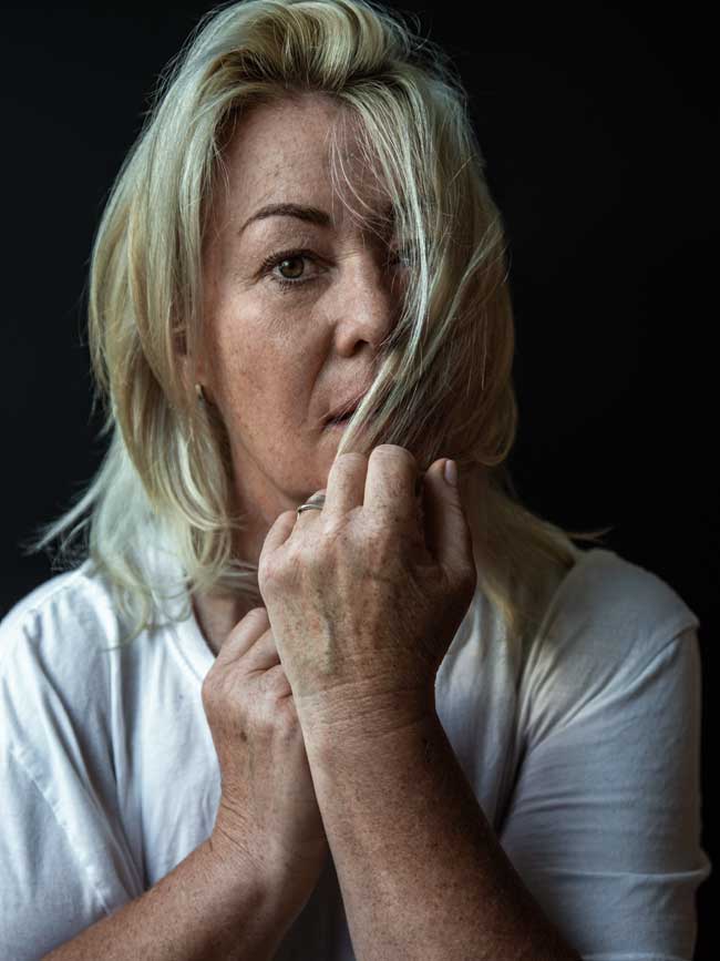 Jann Arden staring in the photographer's direction, pulling several strands of hair toward her mouth with one hand. 
