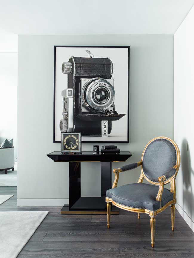 An antique chair sitting in the front hall of a house with a photo of an old camera hanging on the wall behind it. 