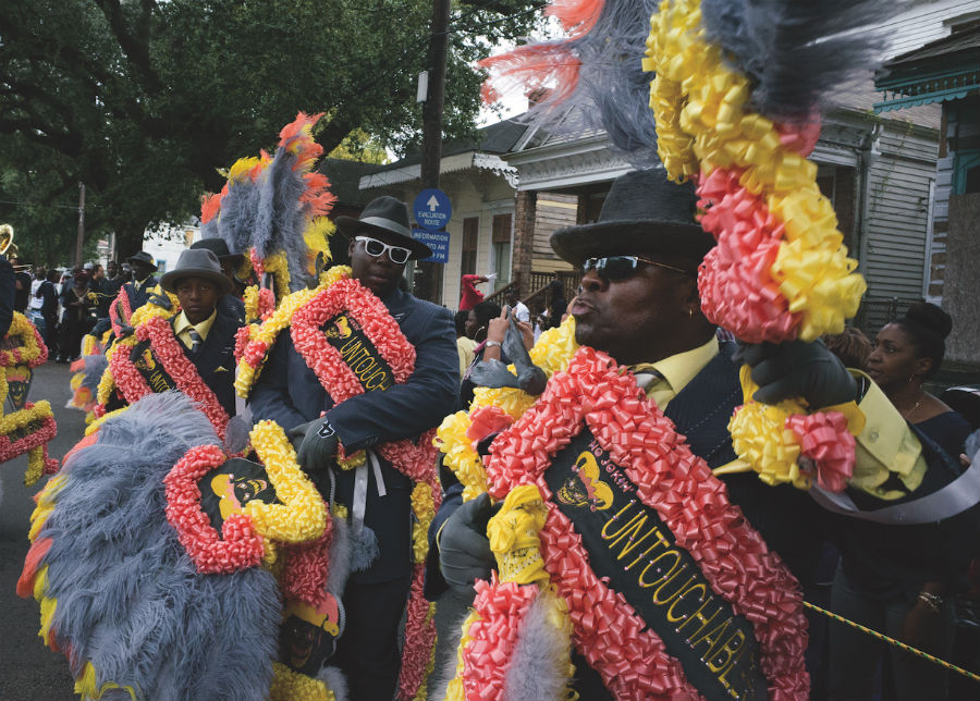 A picture of three men in suits with colourful signs marching in a traditional first line parade.