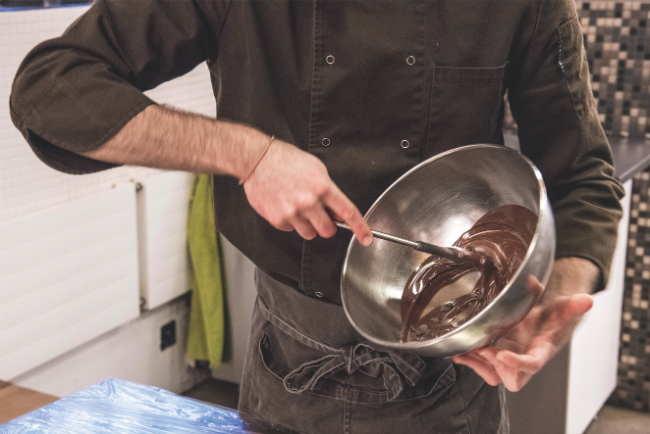 A picture of a man whisking melted chocolate in a silver bowl.