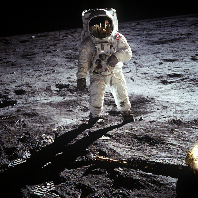 A picture of Buzz Aldrin standing on the moon. Neil Armstrong, the photographer and first man on the moon can be seen in the reflection of Aldrin's visor.