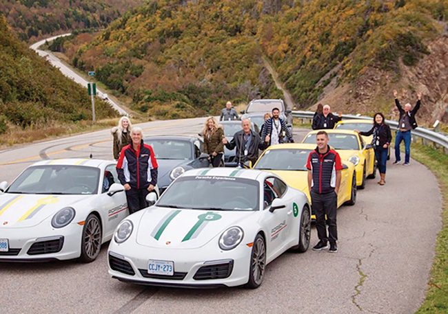 A photo of a group of people standing beside their Porsche cars on the Cabot Trail.